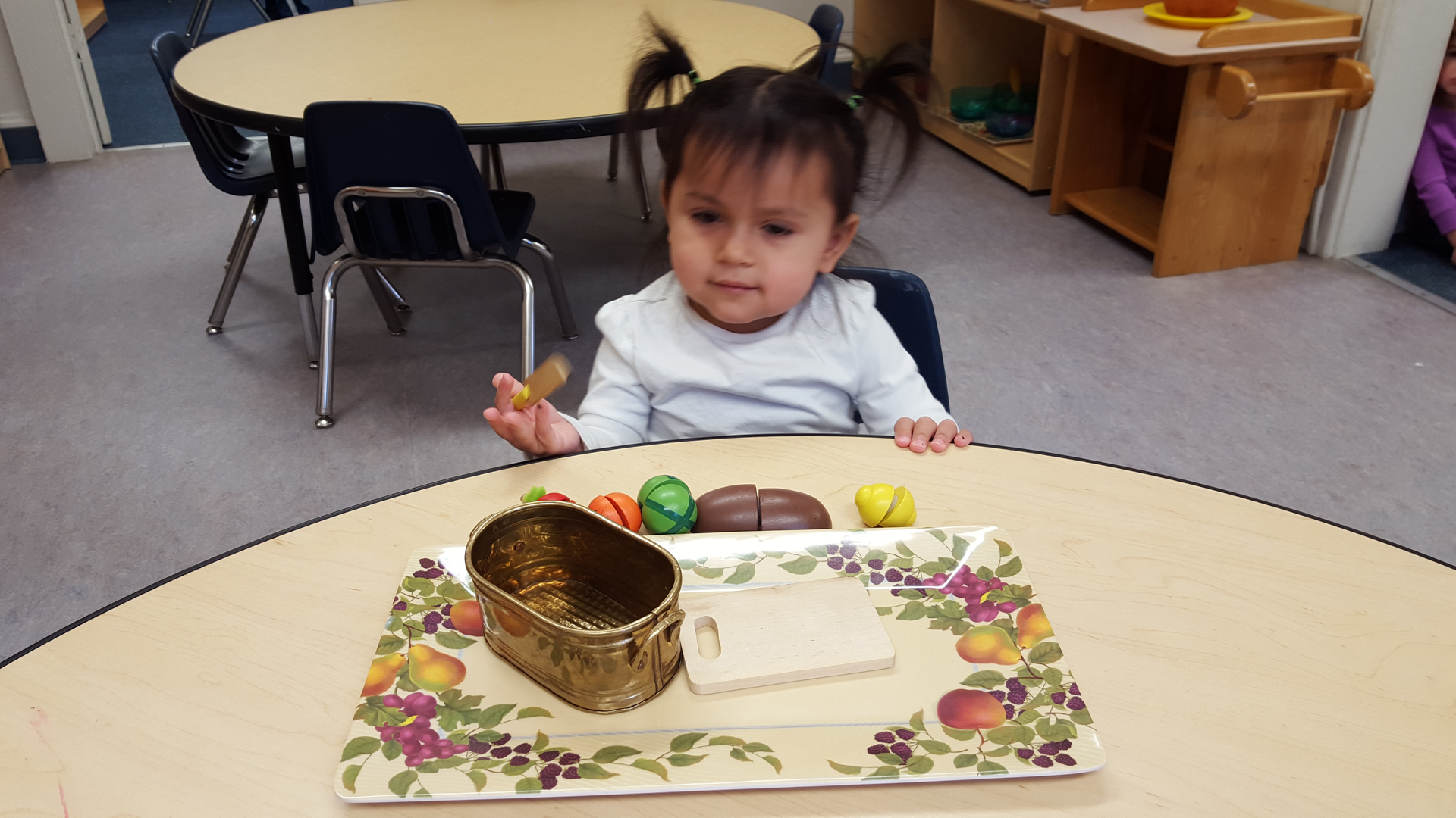 A toddler at a round table with a tray of play food